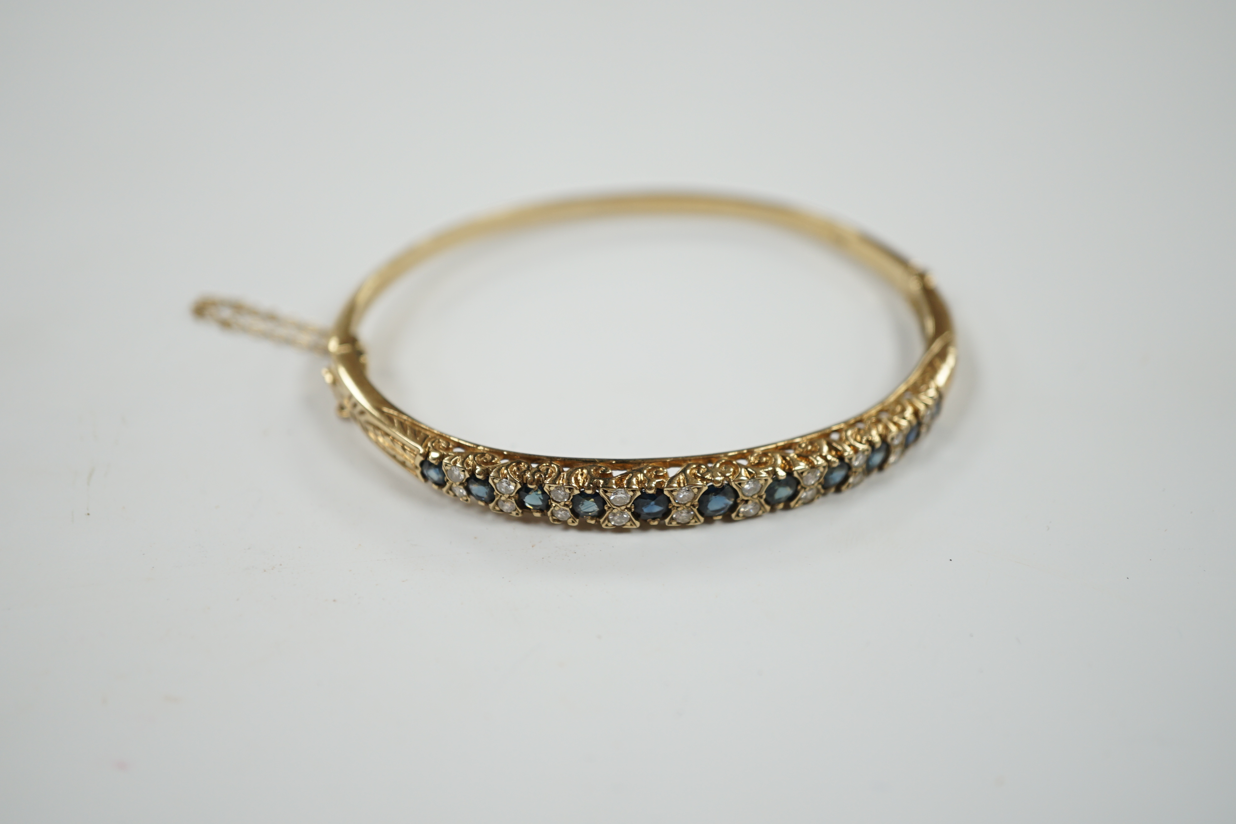 A modern 9ct gold, sapphire and diamond cluster set hinged bangle, gross weight 14 grams.